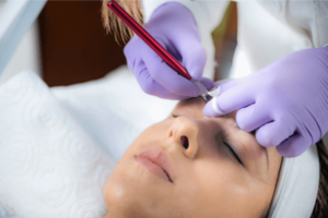 Profissional realizando microblading em cliente, técnica de sobrancelhas com lâminas.